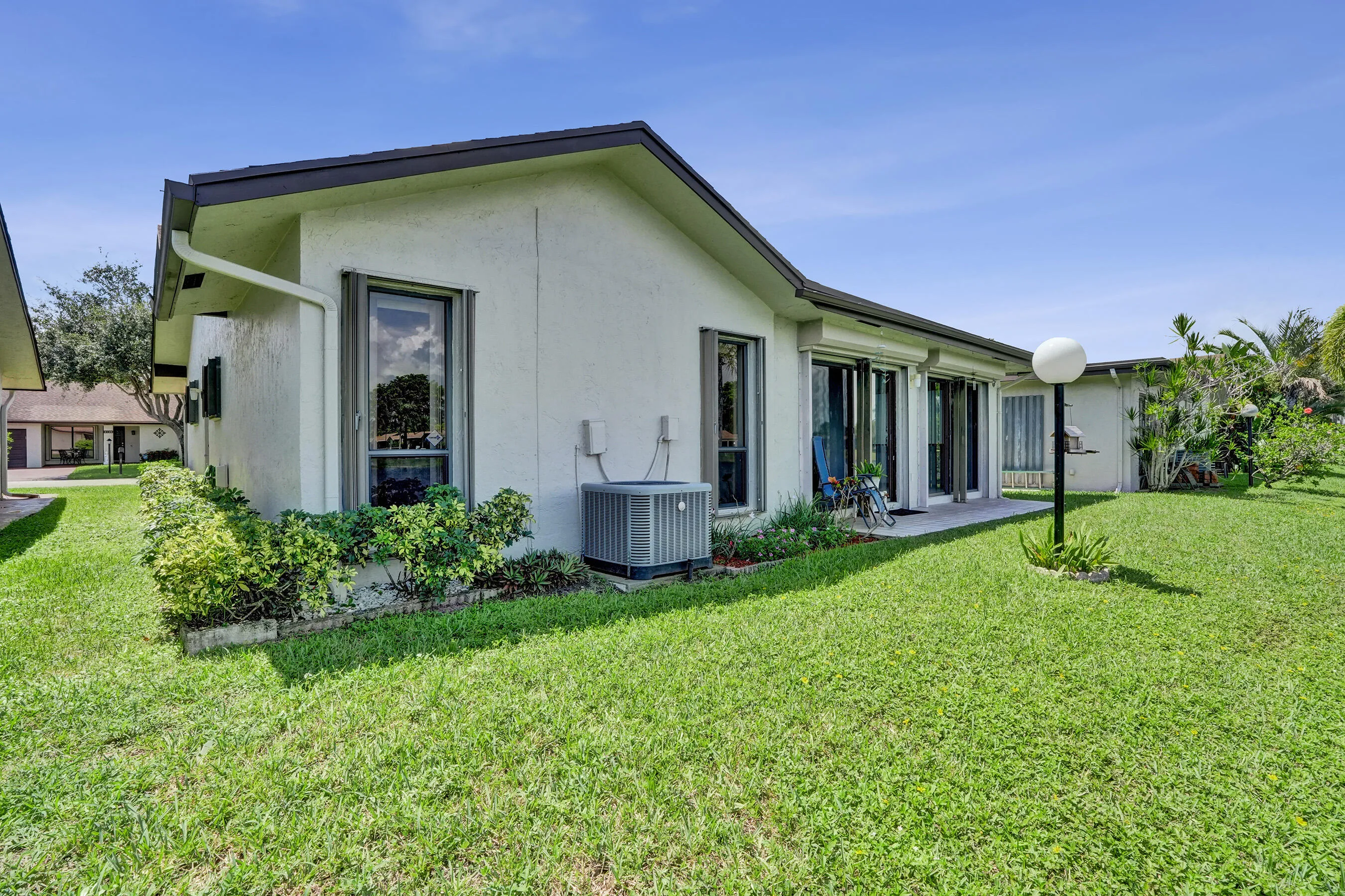 Expansive green lawn, stucco exterior, multiple sliding glass doors, covered patio, and a dedicated outdoor lighting fixture