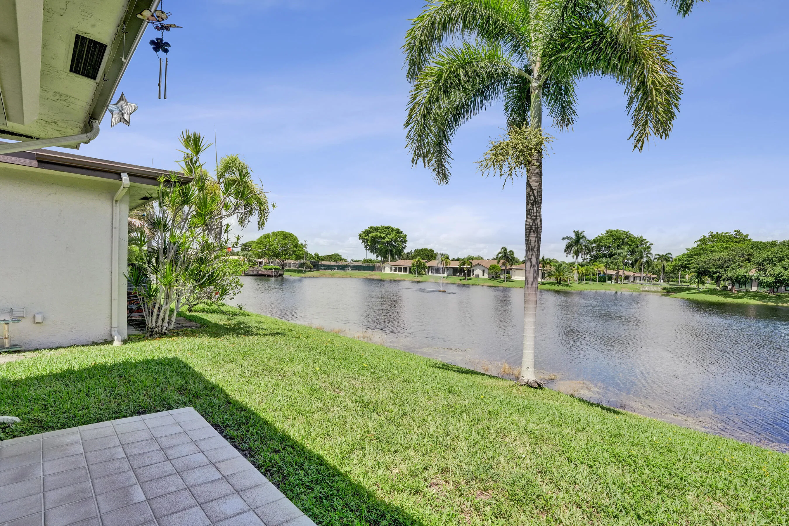 Waterfront exterior with a tiled patio, lush lawn, and mature palm trees