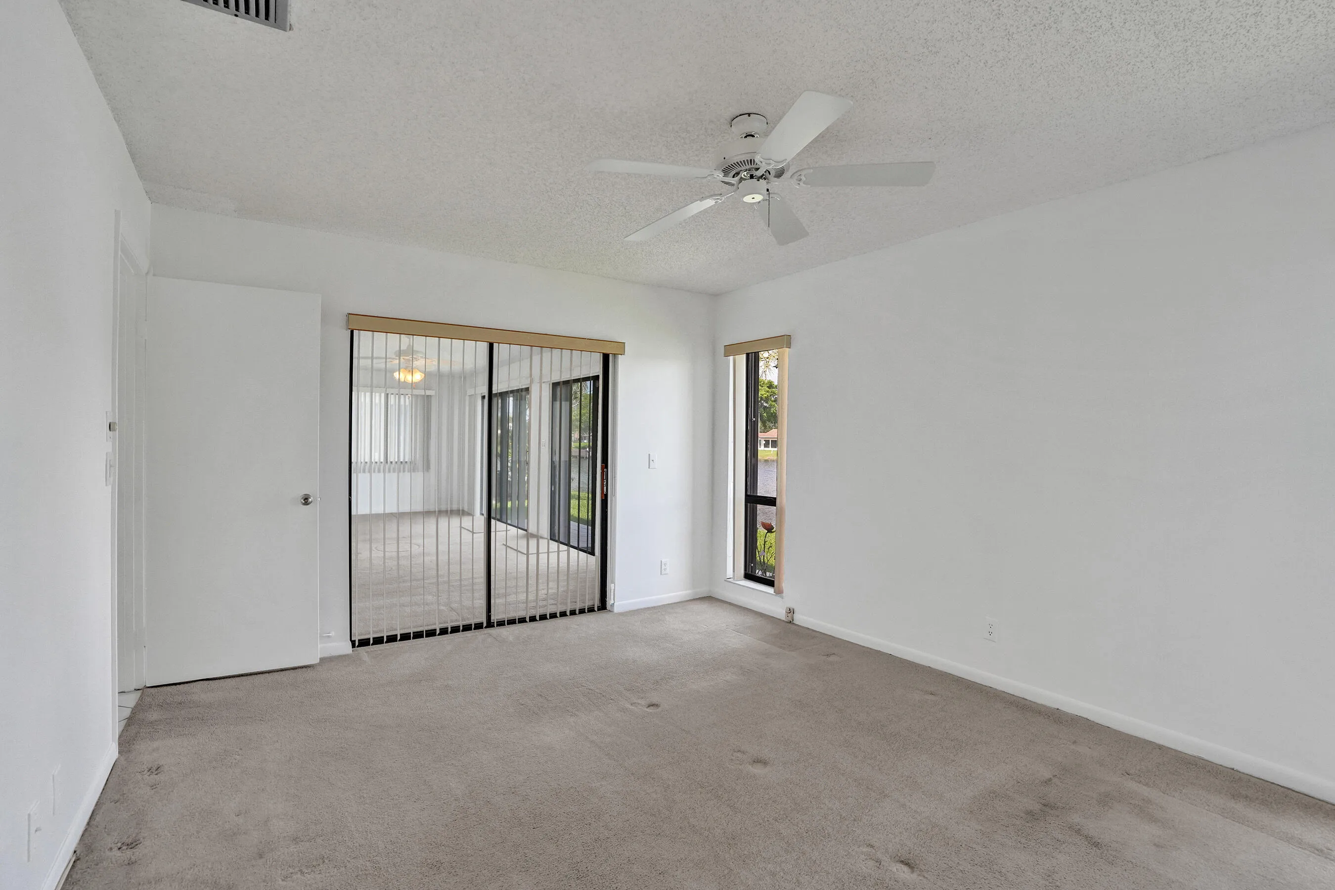 Recessed ceiling fan, textured ceiling, light-colored carpet, sliding glass door with vertical blinds, and a large window