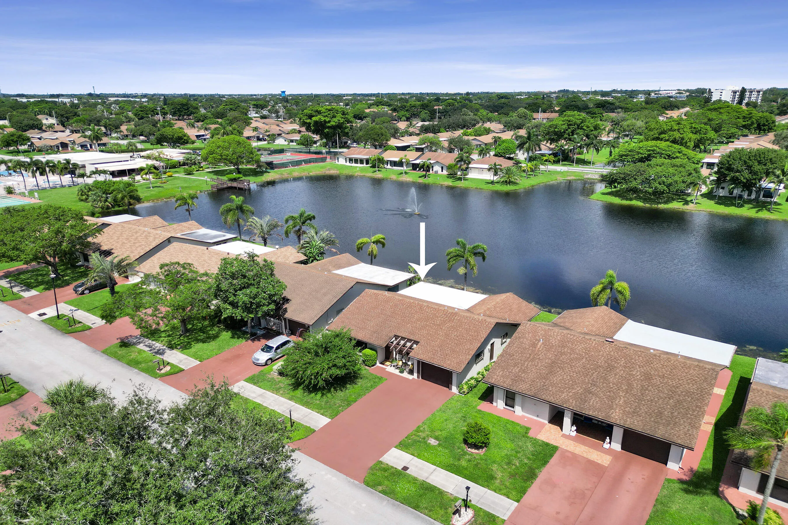 Waterfront property featuring a private paved driveway, an attached garage, and mature landscaping
