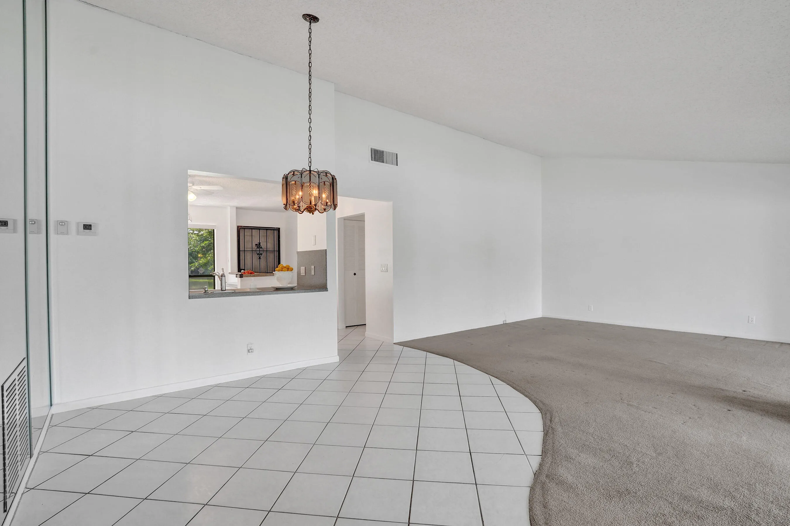 Vaulted ceiling with an attached decorative light fixture, pass-through window, and a combination of tiled and carpeted flooring