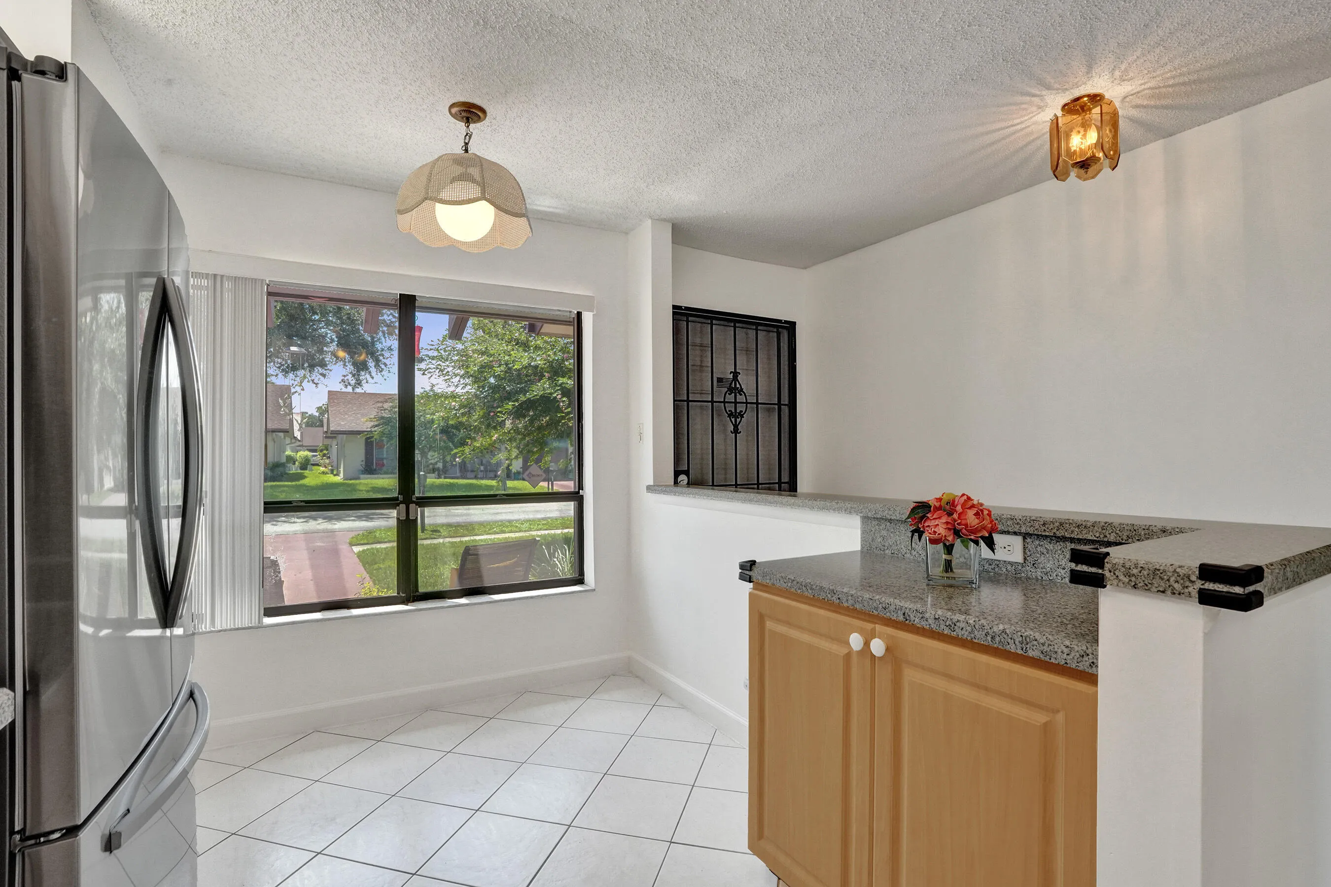 White tile flooring, light wood-finish cabinetry, granite-style countertops, and a large window