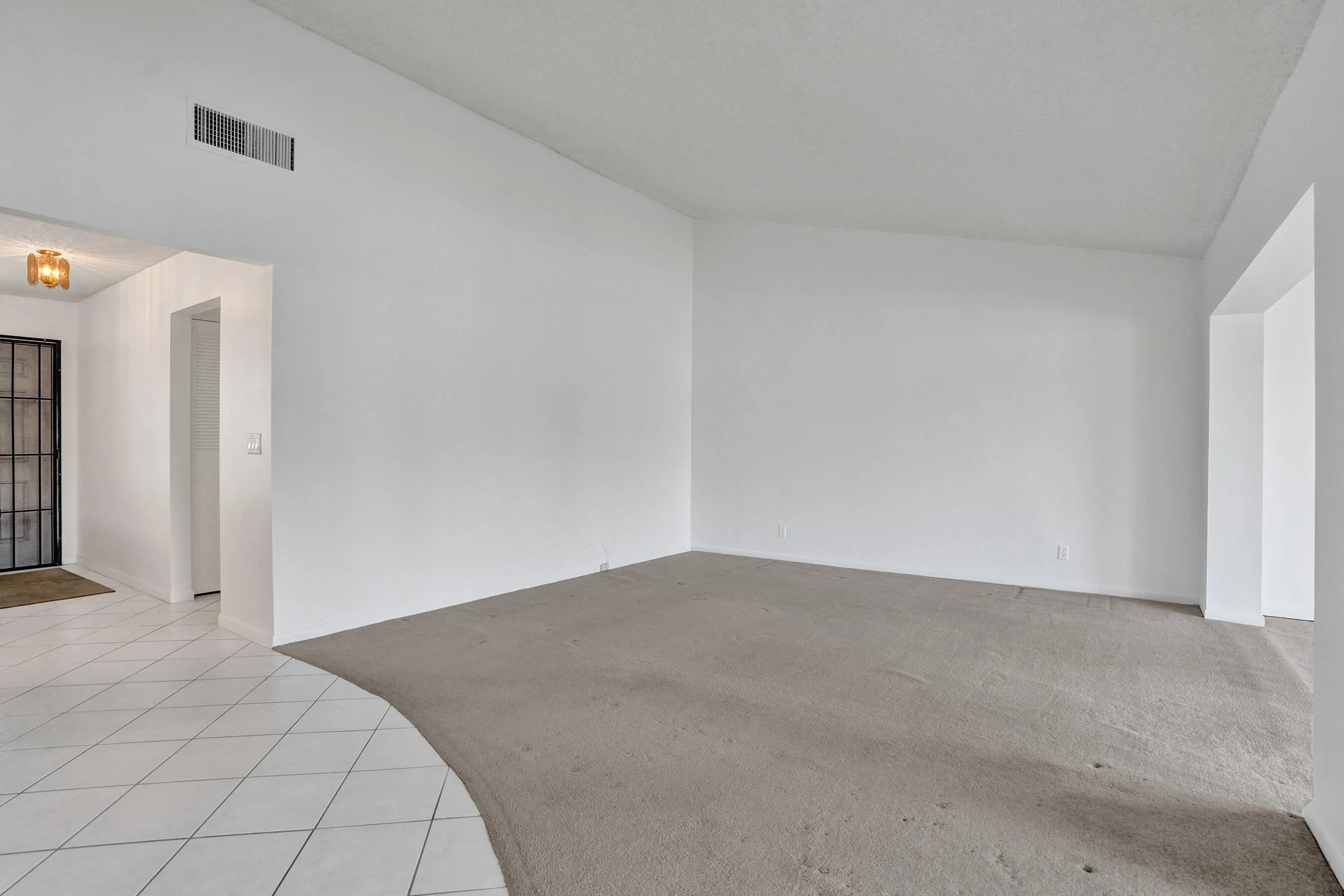 Spacious living area with neutral wall tones, carpeted flooring, and a wide entryway