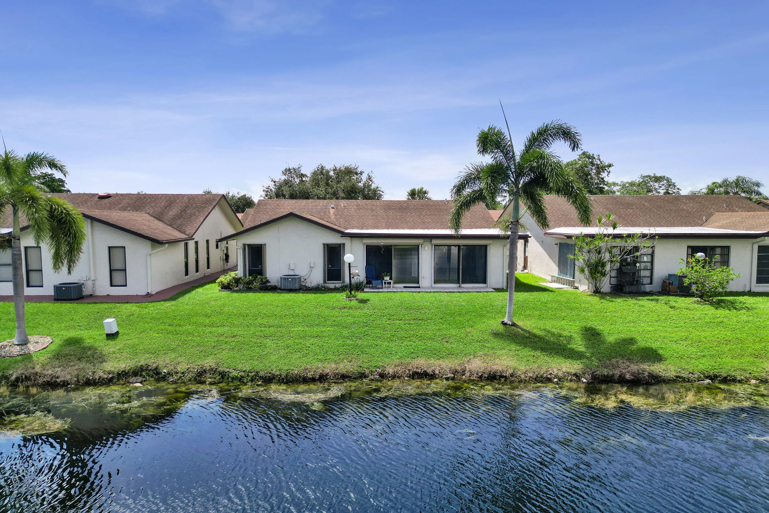 Waterfront property featuring a lush green lawn, mature palm trees, and sliding glass doors