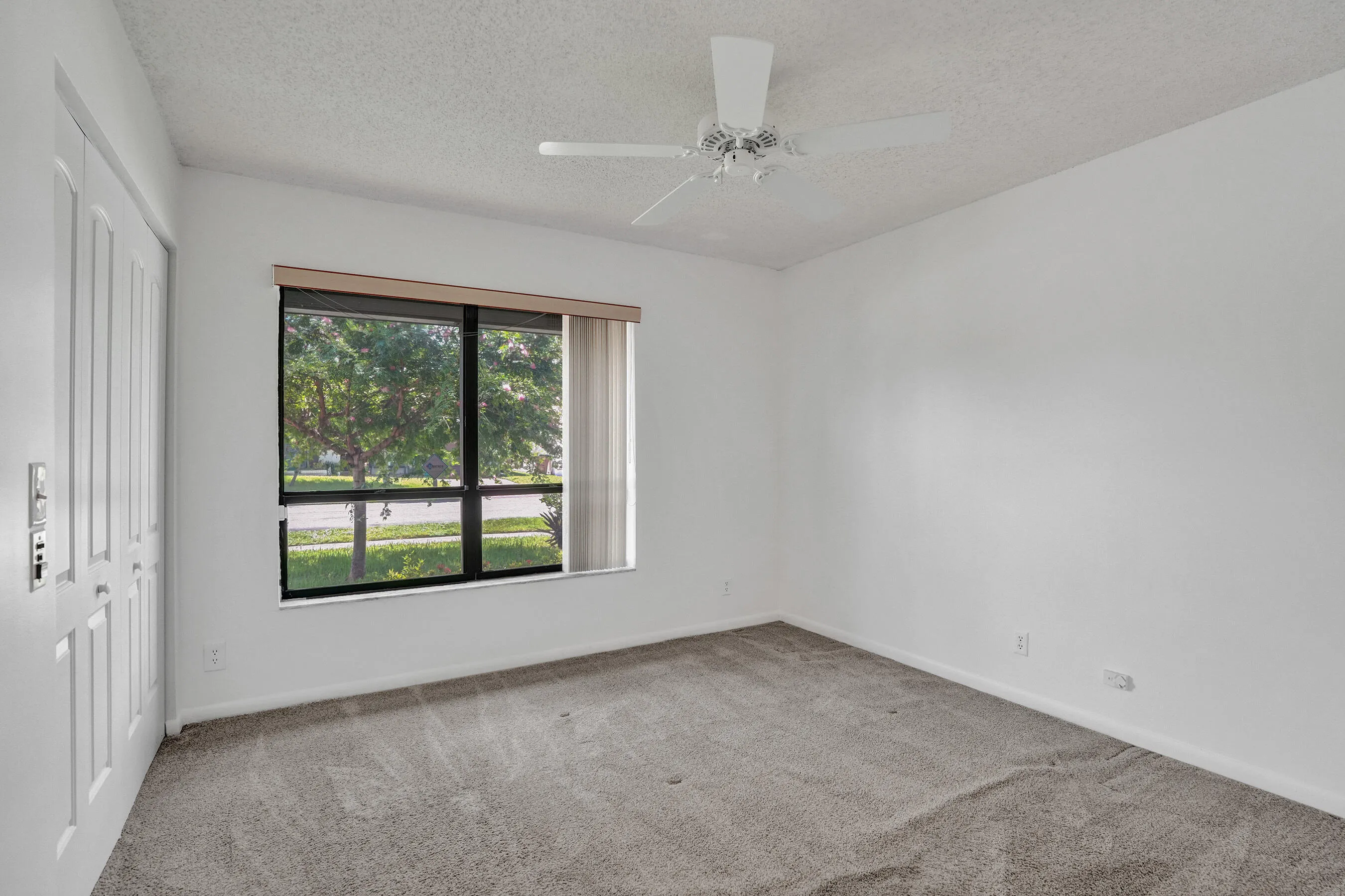 Room with neutral-toned carpeting, a ceiling fan, and a large window with blinds