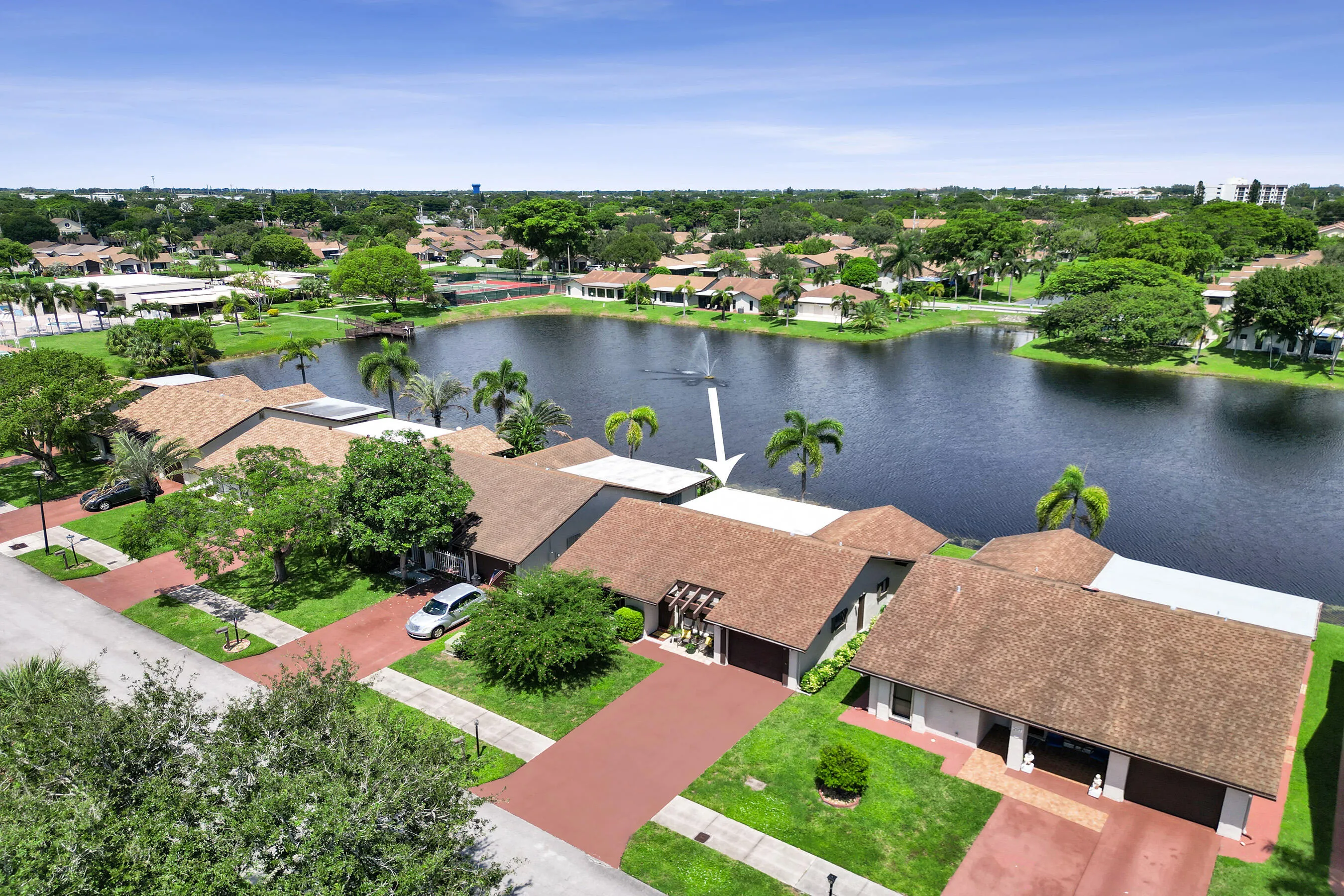 Lakefront property with a red paver driveway, an attached garage, and lush green landscaping