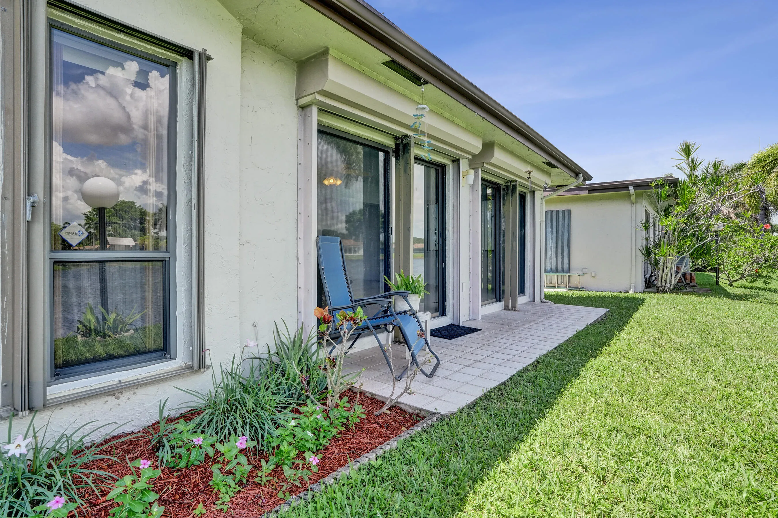 Patio with tiled surface, multiple glass doors, and a landscaped garden bed