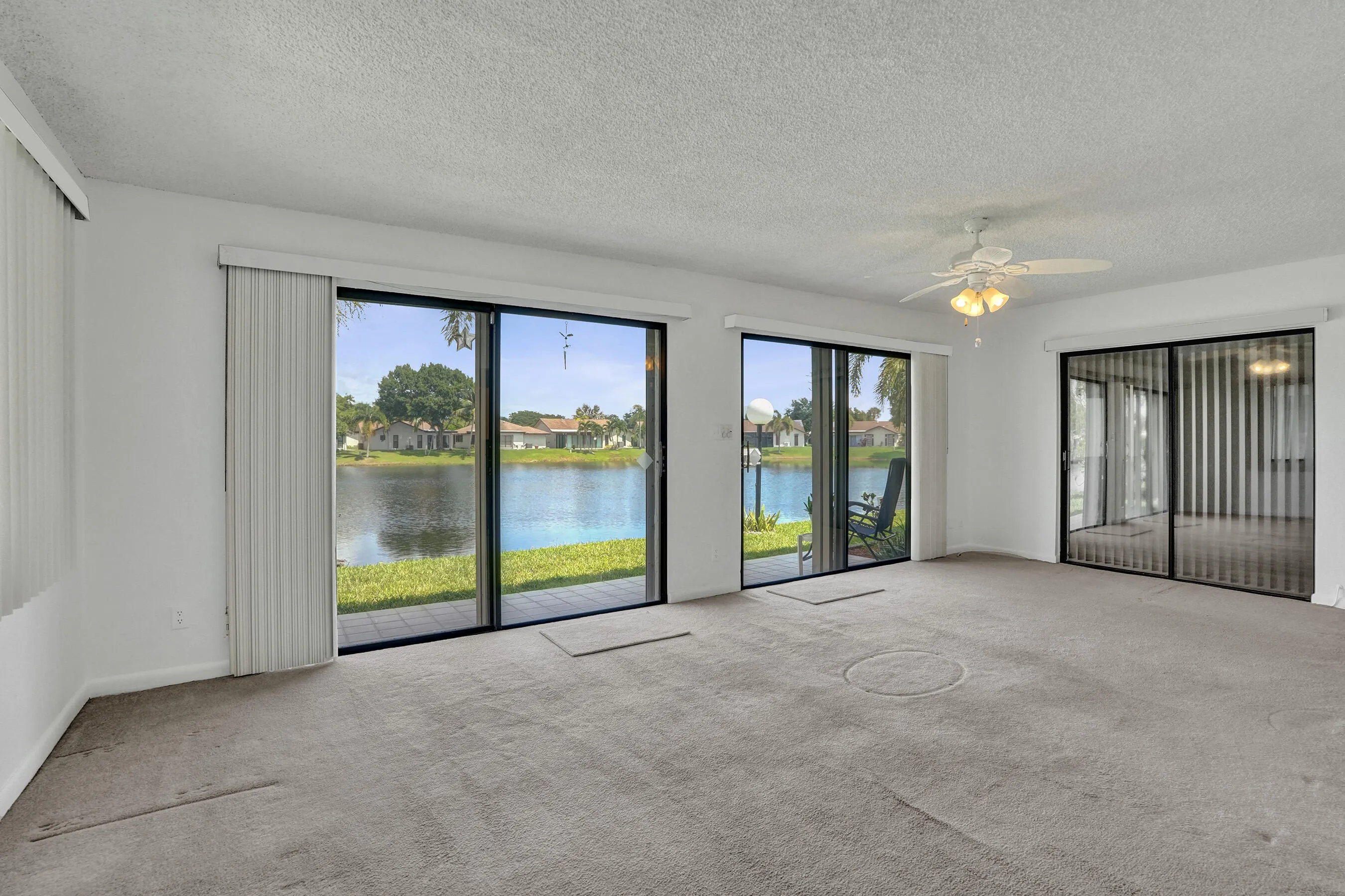 Expansive living space featuring multiple sliding glass doors, textured ceiling, ceiling fan with integrated lighting, and neutral carpet flooring