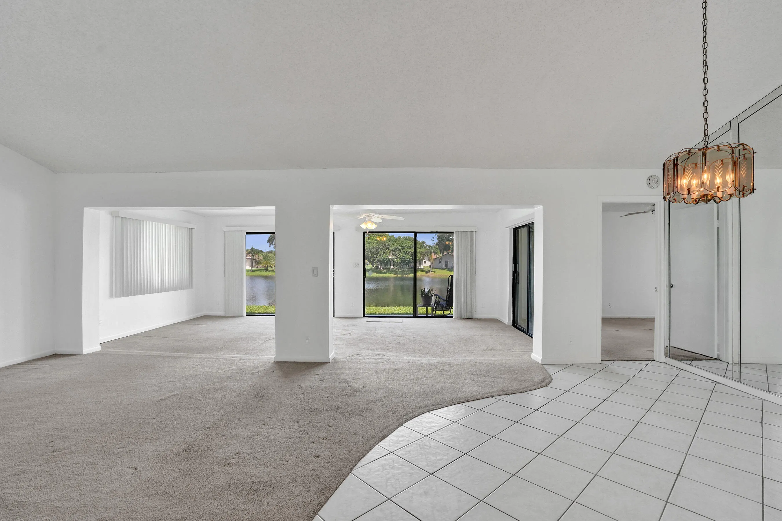 Open concept living space with expansive window walls, white tile flooring, and a decorative ceiling light fixture