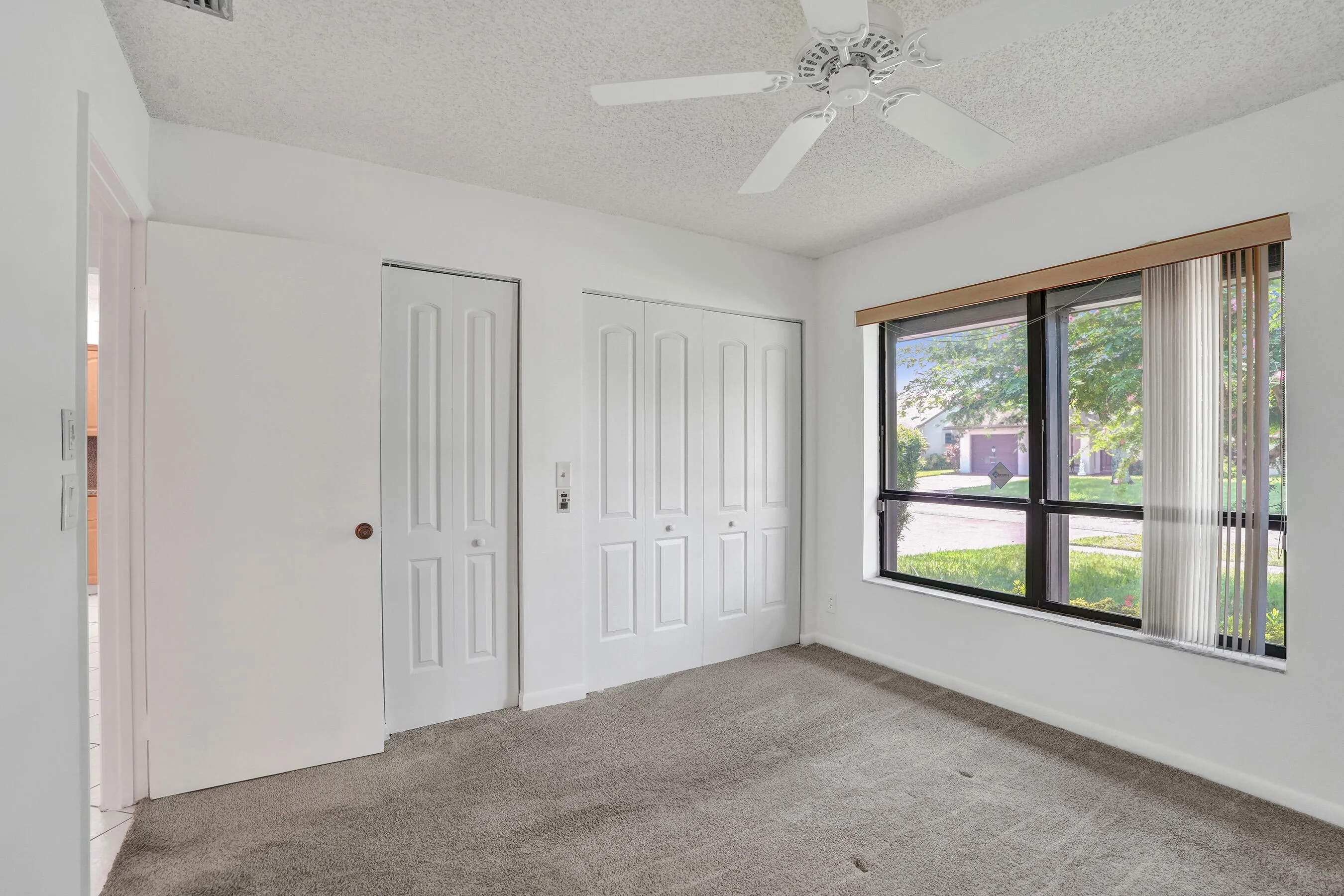 White walls with textured ceiling, ceiling fan, gray carpet flooring, and a large window with vertical blinds