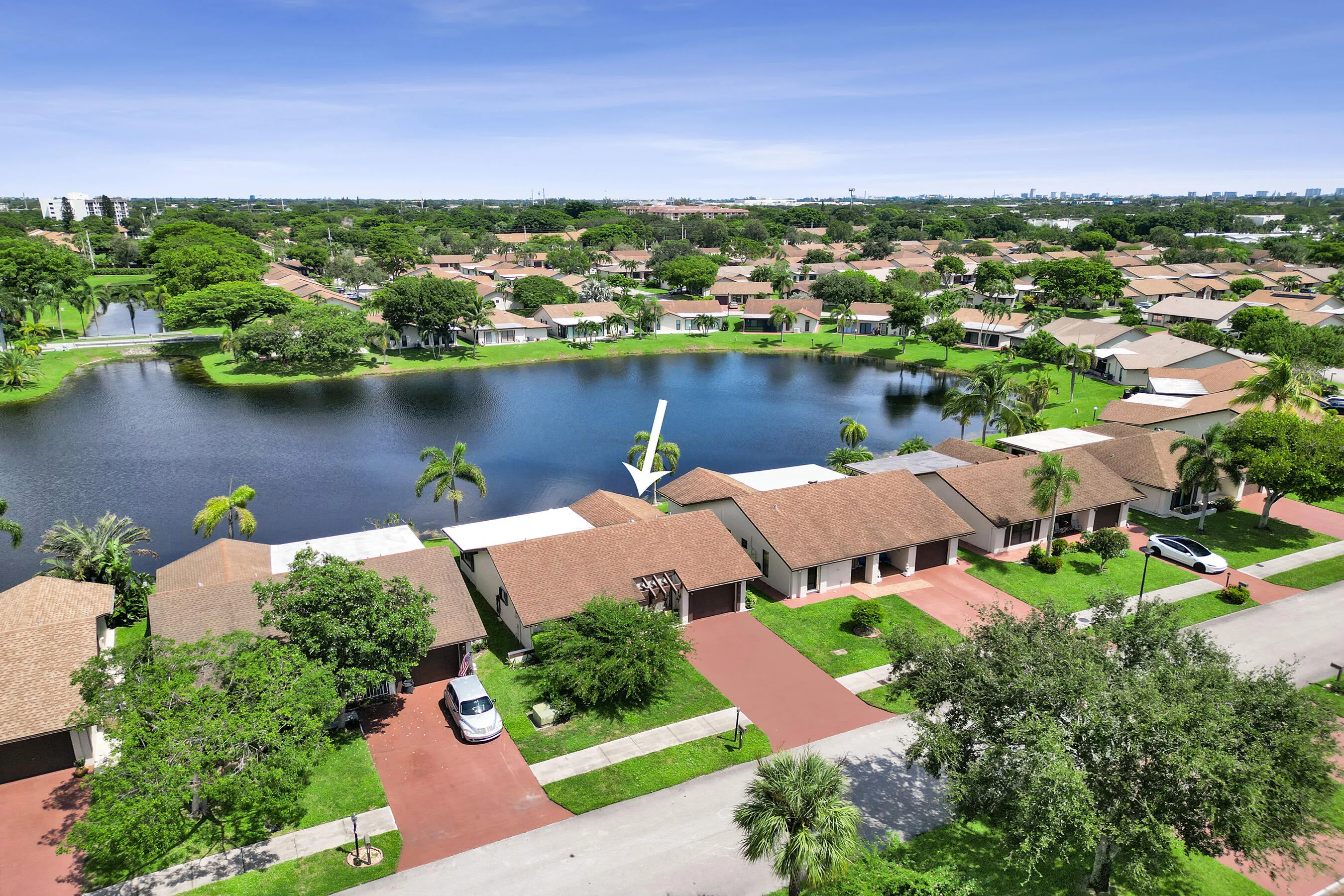 Waterfront property featuring a private paved driveway, attached garage, and mature landscaping