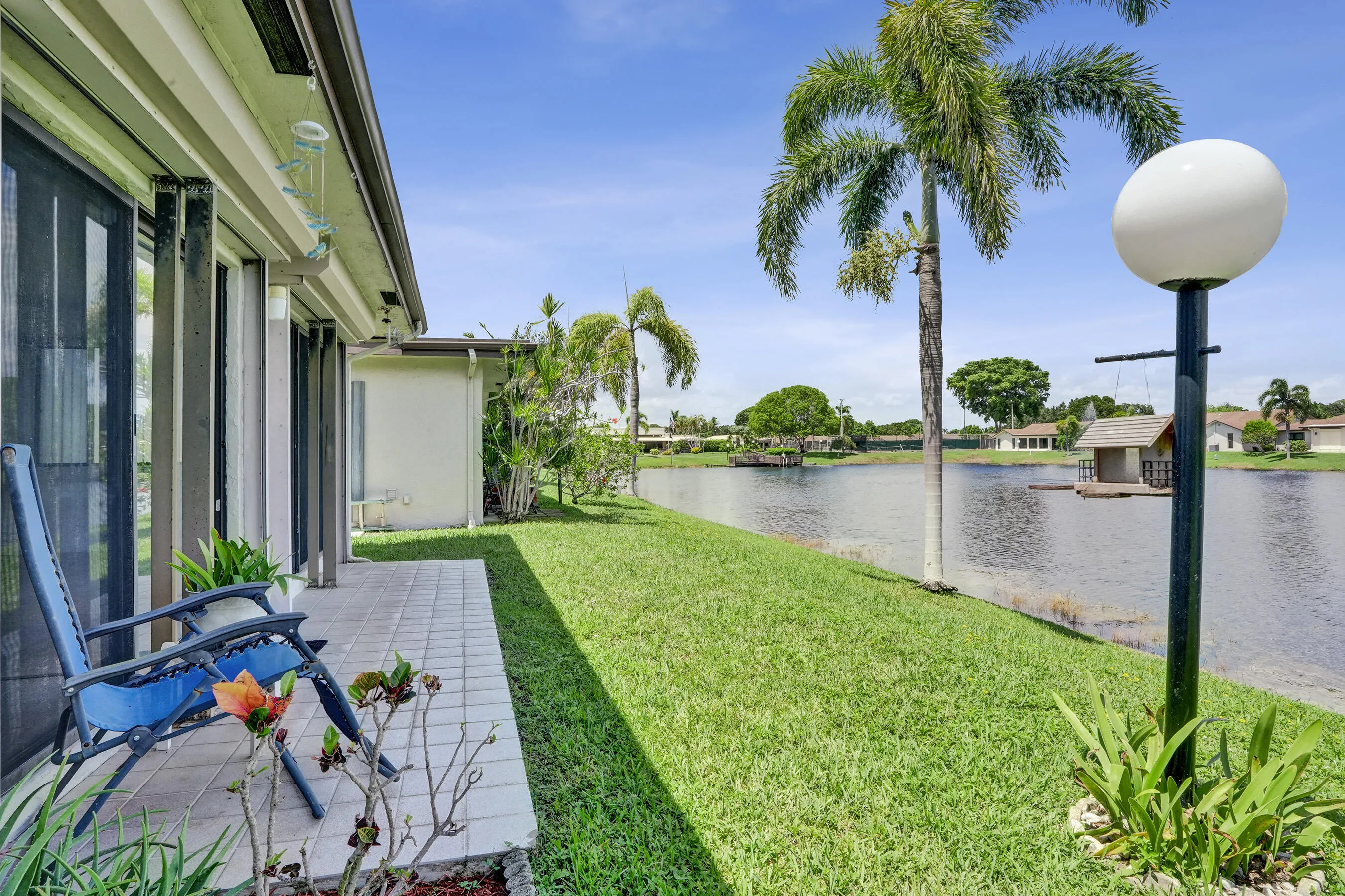 Outdoor patio with tiled flooring, sliding glass doors, and manicured lawn extending to a waterfront