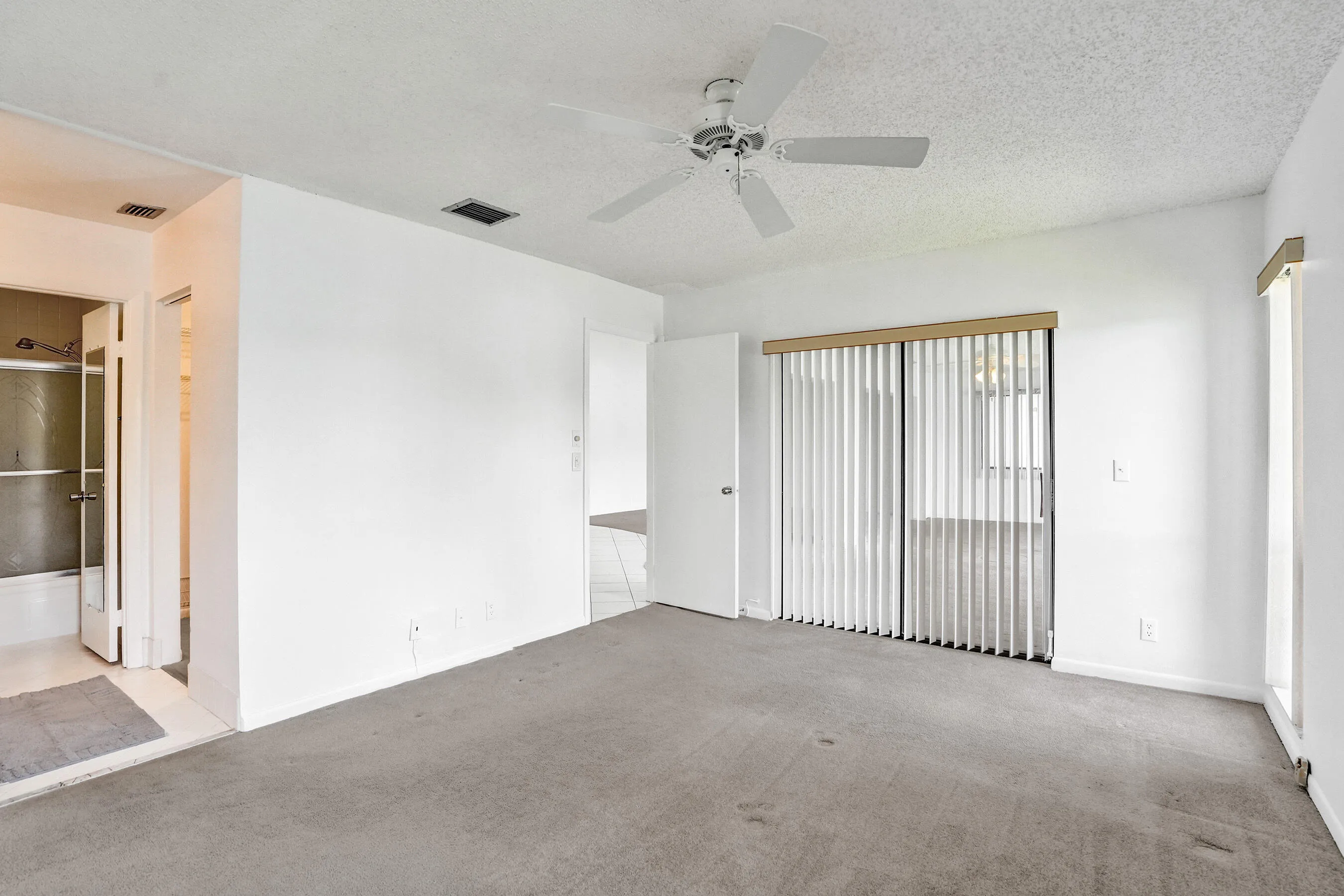 Carpeted interior with a ceiling fan, sliding glass doors with vertical blinds, and white walls