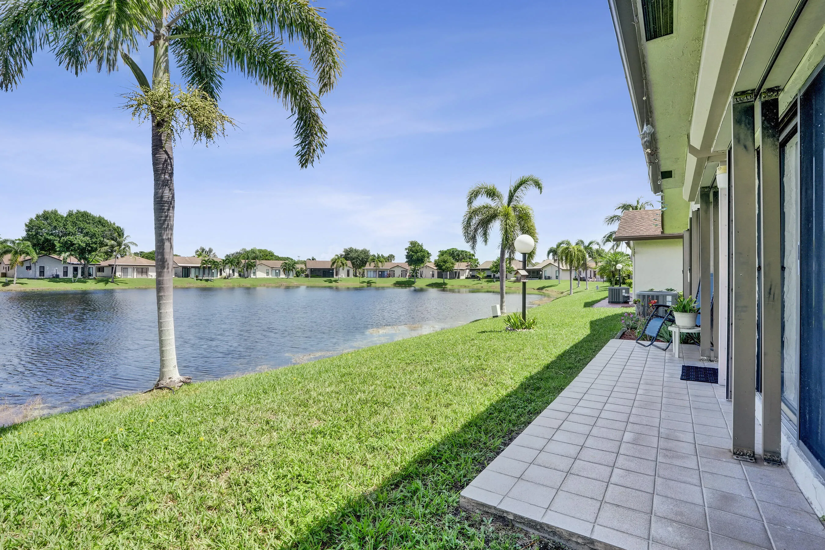 Tiled patio with sliding glass door access, overlooking a substantial body of water with a grass-lined bank