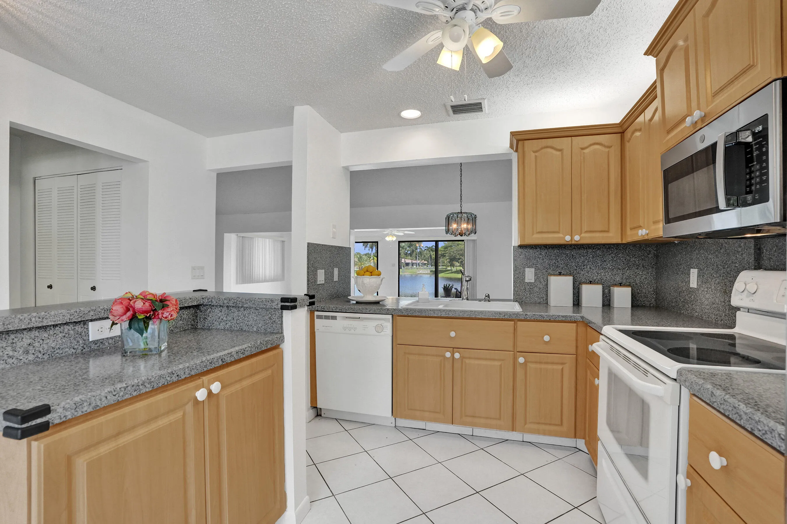 Kitchen featuring wood cabinetry, light-colored countertops, white tile flooring, stainless steel microwave, and white appliances