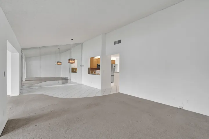 Wall-to-wall mirrored accent wall, two pendant light fixtures, pass-through opening to kitchen, light-colored tile flooring, and carpeted area