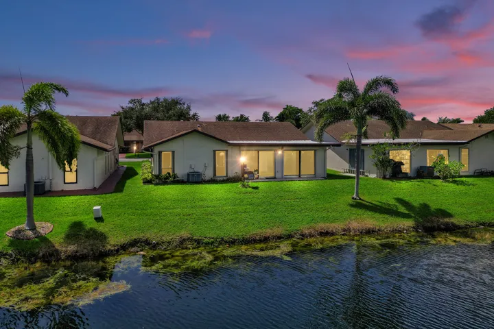 Waterfront property featuring a spacious lawn, mature palm trees, and a patio with sliding glass doors