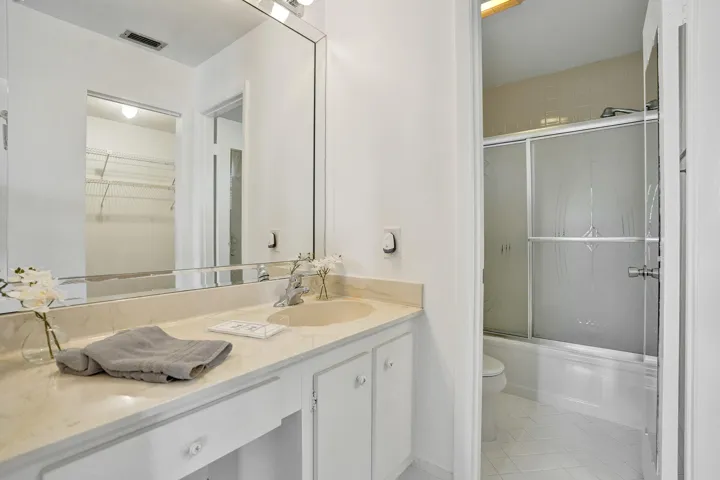 Vanity with integrated sink and stone-look countertop, large vanity mirror, white cabinetry with decorative pulls, and a shower-tub combination with frosted sliding glass doors