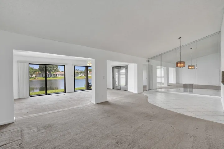 Lakefront sliding glass doors, carpeted living area, tile flooring, mirrored wall, and two pendant light fixtures