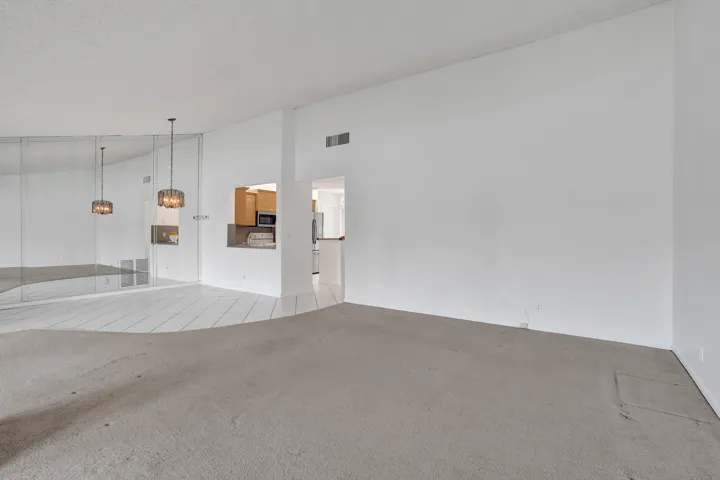 Wall-to-wall mirrored accent wall, two suspended light fixtures, kitchen pass-through window with solid surface countertop, and mixed flooring with carpet and tile