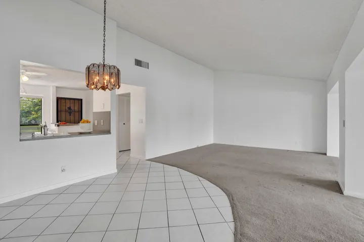 Vaulted ceiling with an ornate hanging light fixture, white tile flooring, and a pass-through window to the kitchen