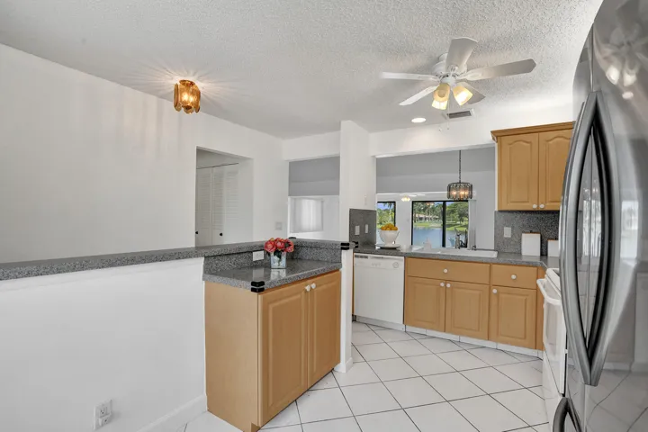 Kitchen featuring light wood cabinetry, white tile flooring, granite-finish countertops, and a stainless steel refrigerator