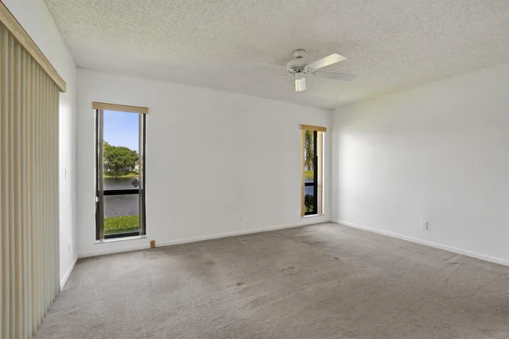 Expansive room featuring two vertical windows, a ceiling fan, and light-colored carpeting