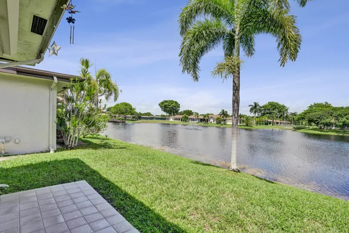 Waterfront exterior with a tiled patio, lush lawn, and mature palm trees