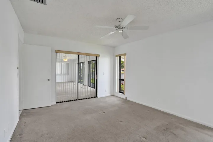 Recessed ceiling fan, textured ceiling, light-colored carpet, sliding glass door with vertical blinds, and a large window