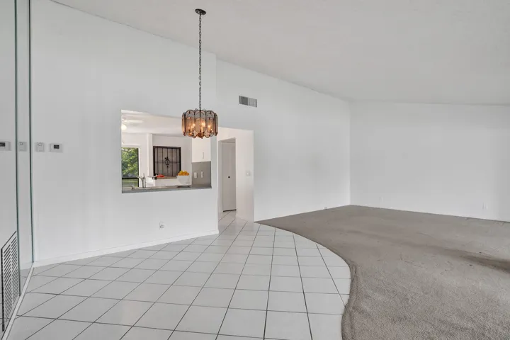Vaulted ceiling with an attached decorative light fixture, pass-through window, and a combination of tiled and carpeted flooring