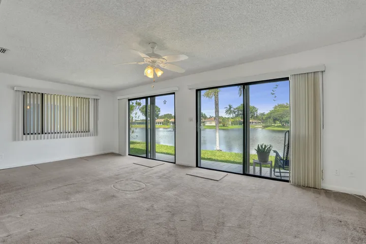 Sliding glass doors opening to outdoor space, ceiling fan with integrated lighting, window with vertical blinds, and textured ceiling