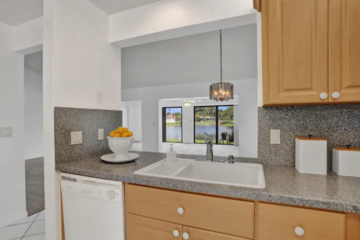Kitchen pass-through with a double basin sink, light wood-finish cabinetry, and speckled countertops