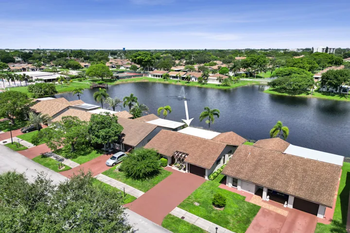 Lakefront property with a red paver driveway, an attached garage, and lush green landscaping