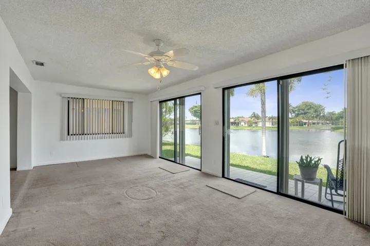 Sliding glass doors opening to a patio, a ceiling fan with integrated lighting, and a large window with vertical blinds