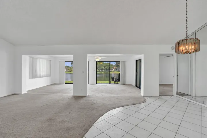 Open concept living space with expansive window walls, white tile flooring, and a decorative ceiling light fixture