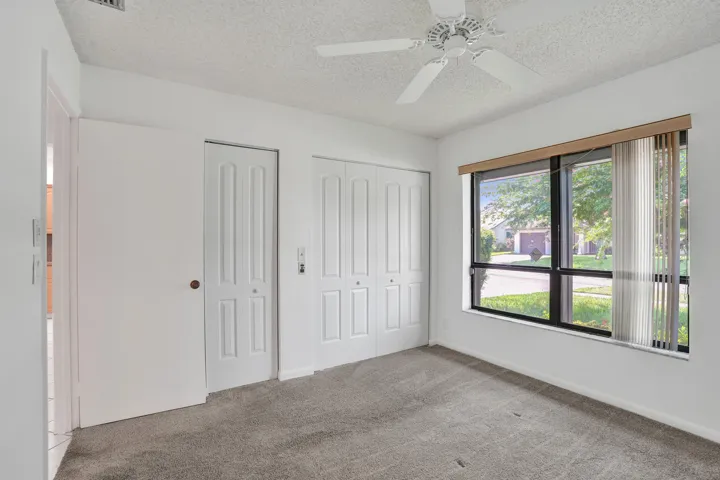 White walls with textured ceiling, ceiling fan, gray carpet flooring, and a large window with vertical blinds