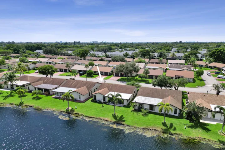 Waterfront property with a lush green lawn, mature palm trees, and a paved driveway