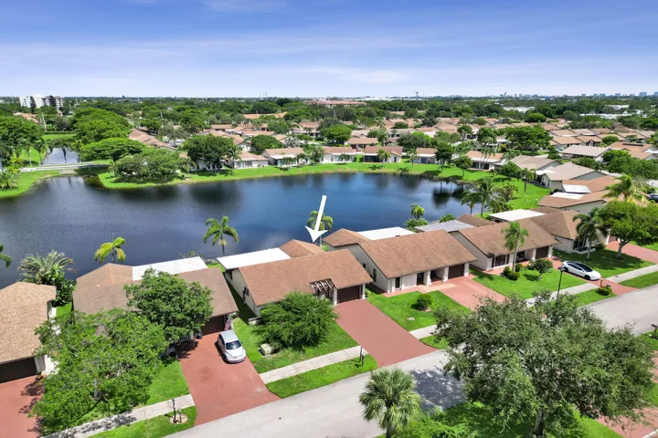Waterfront property featuring a private paved driveway, attached garage, and mature landscaping