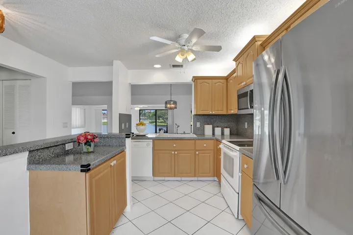 Kitchen with natural wood cabinetry, stone countertops, stainless steel appliances, and diagonal tile flooring