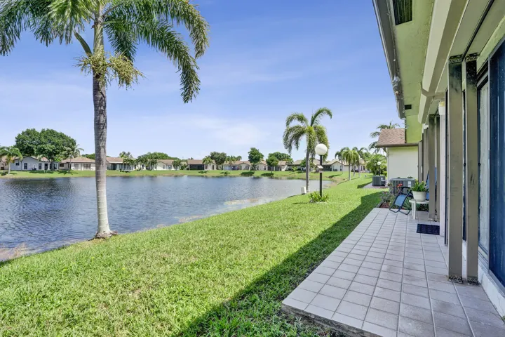 Tiled patio with sliding glass door access, overlooking a substantial body of water with a grass-lined bank