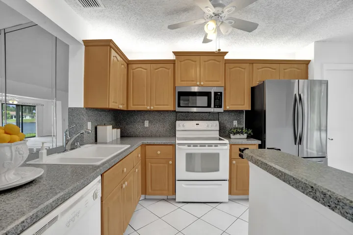 Kitchen featuring light wood cabinetry, white appliances, stainless steel refrigerator and microwave, and grey countertops