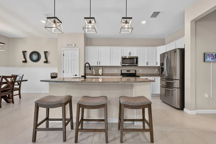 Kitchen featuring white shaker cabinetry, stainless steel appliances, a center island with a granite-style countertop, and pendant lighting