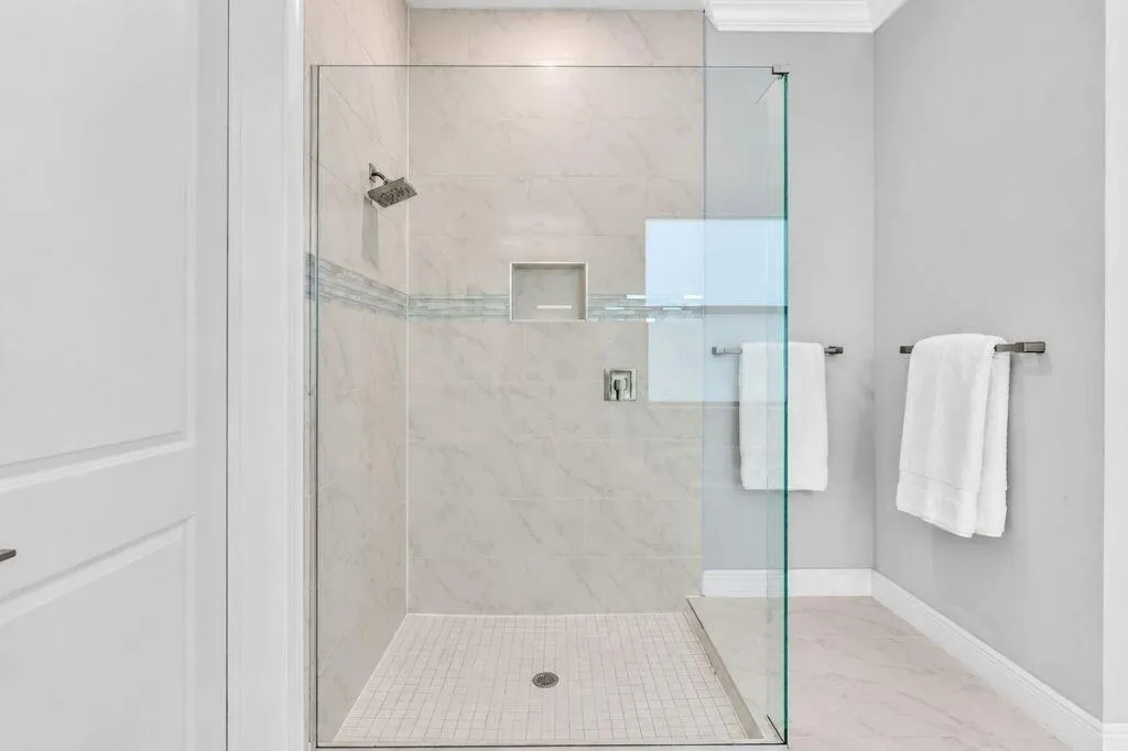 Glass-enclosed shower featuring large format wall tiles, a built-in niche, and a contrasting mosaic tile accent band