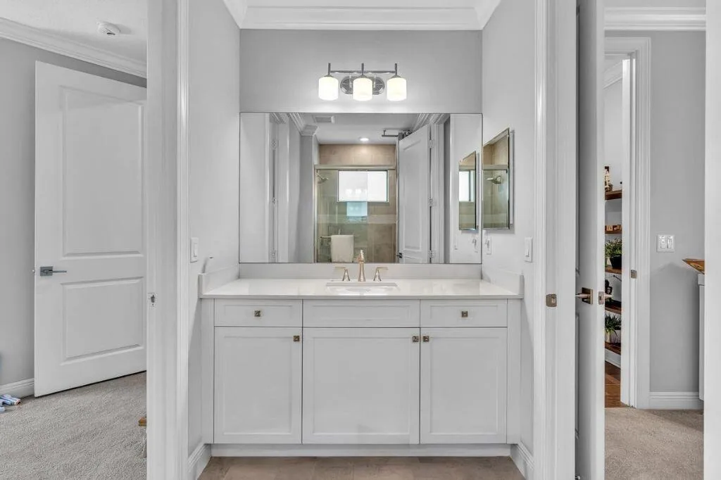 Bathroom vanity featuring white cabinetry, a light-toned countertop, and an integrated rectangular sink with a gold-tone faucet