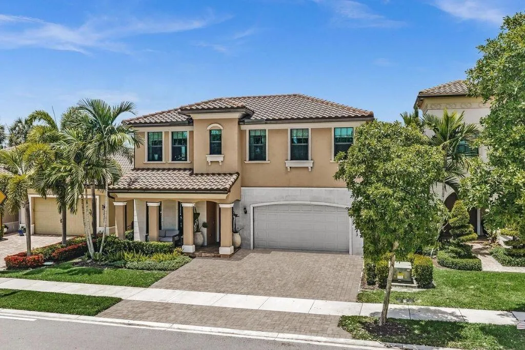 Mediterranean-style residence featuring a tile roof, stucco exterior, two-car garage, paver driveway, and mature palm trees