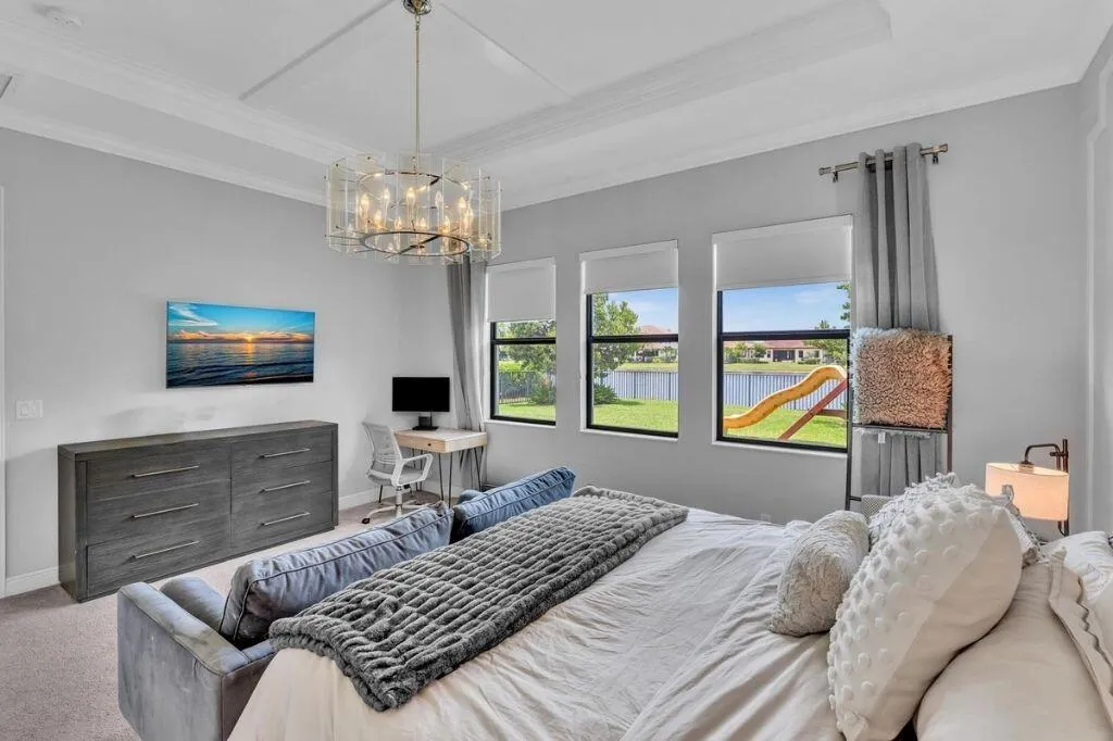 Spacious interior featuring a coffered ceiling with a decorative chandelier, multiple windows with roller shades, and a built-in desk area