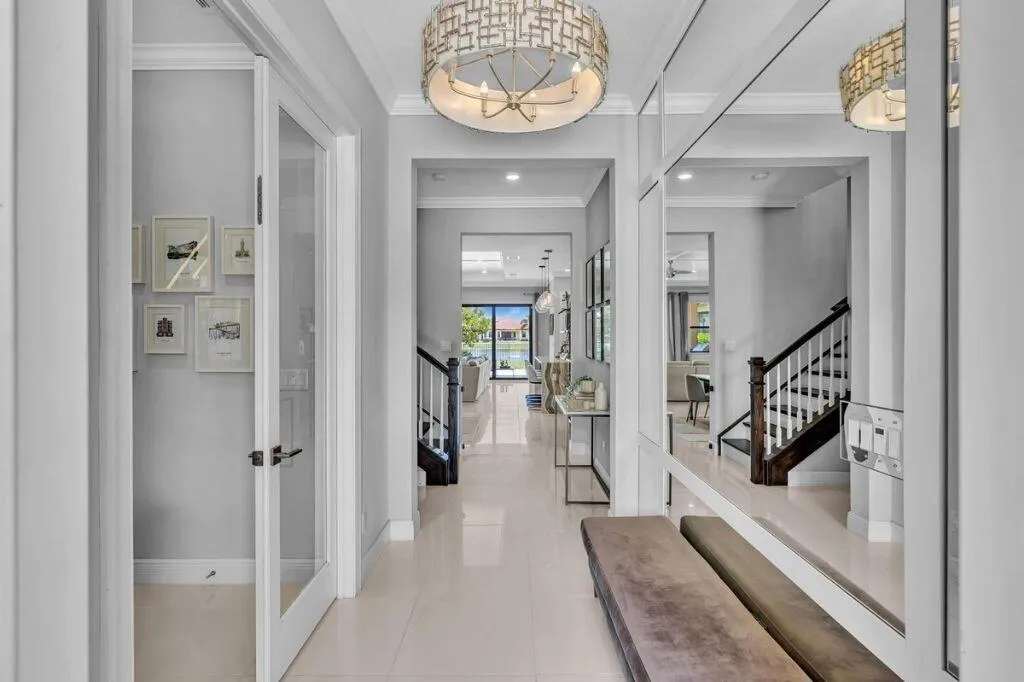 Grand entryway featuring a decorative ceiling fixture, tiled flooring, glass-paneled interior doors, and a dark wood-finish staircase with white risers