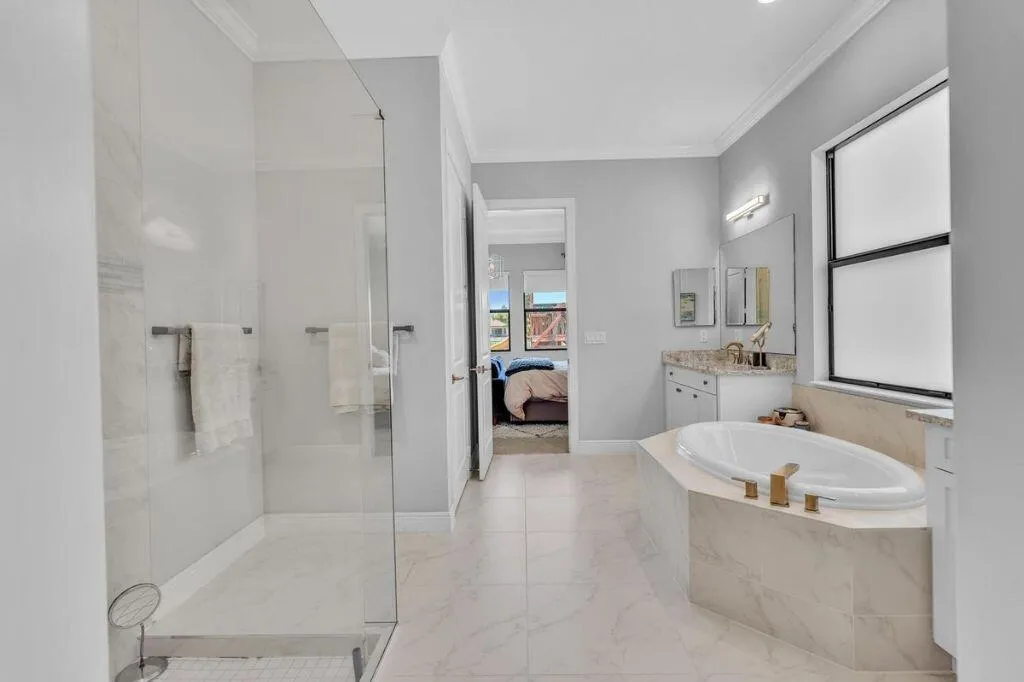 Spacious bathroom featuring a frameless glass shower enclosure, a built-in soaking tub with gold-tone fixtures, a vanity with a stone countertop, and tile flooring