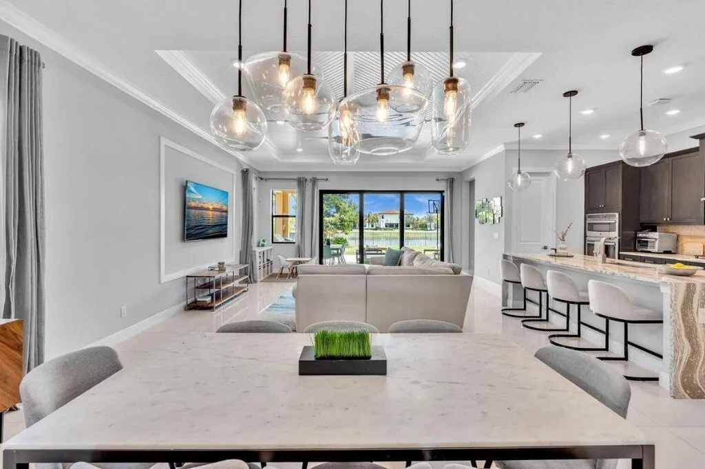 Spacious open-concept interior featuring light tile flooring, an ornate tray ceiling with contemporary pendant lighting, and a kitchen island with stone detailing
