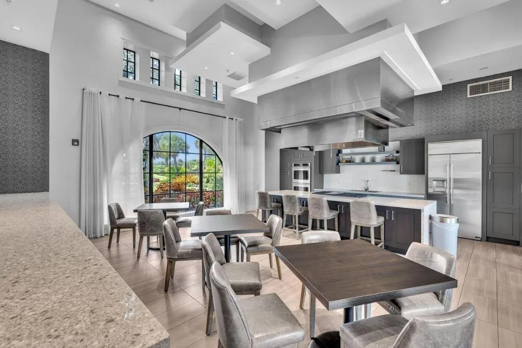Spacious kitchen and dining area featuring a large arched window, vaulted ceilings, a substantial kitchen island with seating, a commercial-grade range hood, and integrated stainless steel appliances